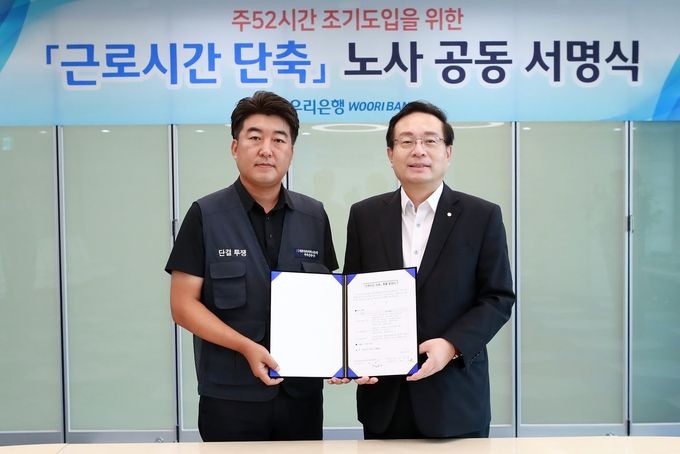 우리은행 노사는 시중은행 최초로 주52시간 근무제를 10월에 조기 도입하기로 합의했다. 손태승 은행장(사진 오른쪽)과 박필준 노조위원장이 ‘주52시간 조기도입을 위한 노사 공동 서명식’을 실시한 후 기념 촬영을 하고 있다.