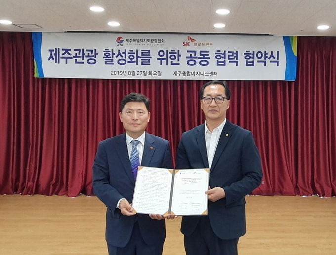 장창훈 SK브로드밴드 기업고객1본부장(왼쪽)과 김남진 제주관광협회 상근이사가 27일 제주관광협회 제주종합비즈니스센터에서 업무협약 체결과 기념촬영 하고 있다. 사진=SK브로드밴드