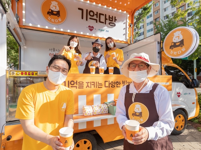 한독과 서울시는 20일 성동구 동마장 어린이 공원에서 치매 인식 개선 캠페인을 위한 ‘기억다방(기억을 지키는 다양한 방법)’ 공동 캠페인을 진행했다. ‘기억다방’ 행사에 바리스타로 참여한 어르신과 함께 한독 임직원들이 기억다방 이동형 카페 앞에서 포즈를 취하고 있다.(사진=한독)