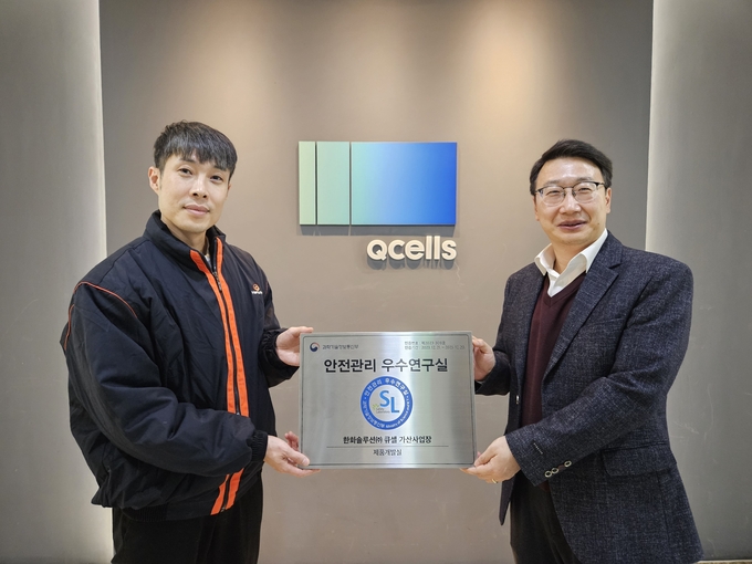 한화큐셀 박정필 시스템개발센터장(우)과 정상민 제품개발팀장이 서울 금천구 시스템개발센터에서 ‘안전관리 우수연구실’ 인증패를 들고 기념 촬영을 하고 있다.(사진=한화큐셀)